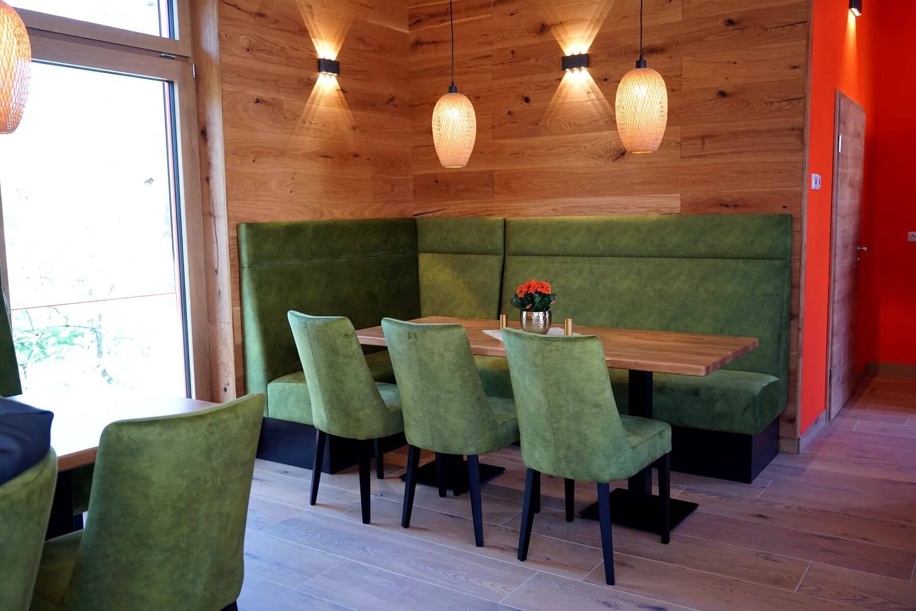 Gastraum im Cafe Flow mit gruenen Polsterstuehlen und Polsterbank an Holzwand