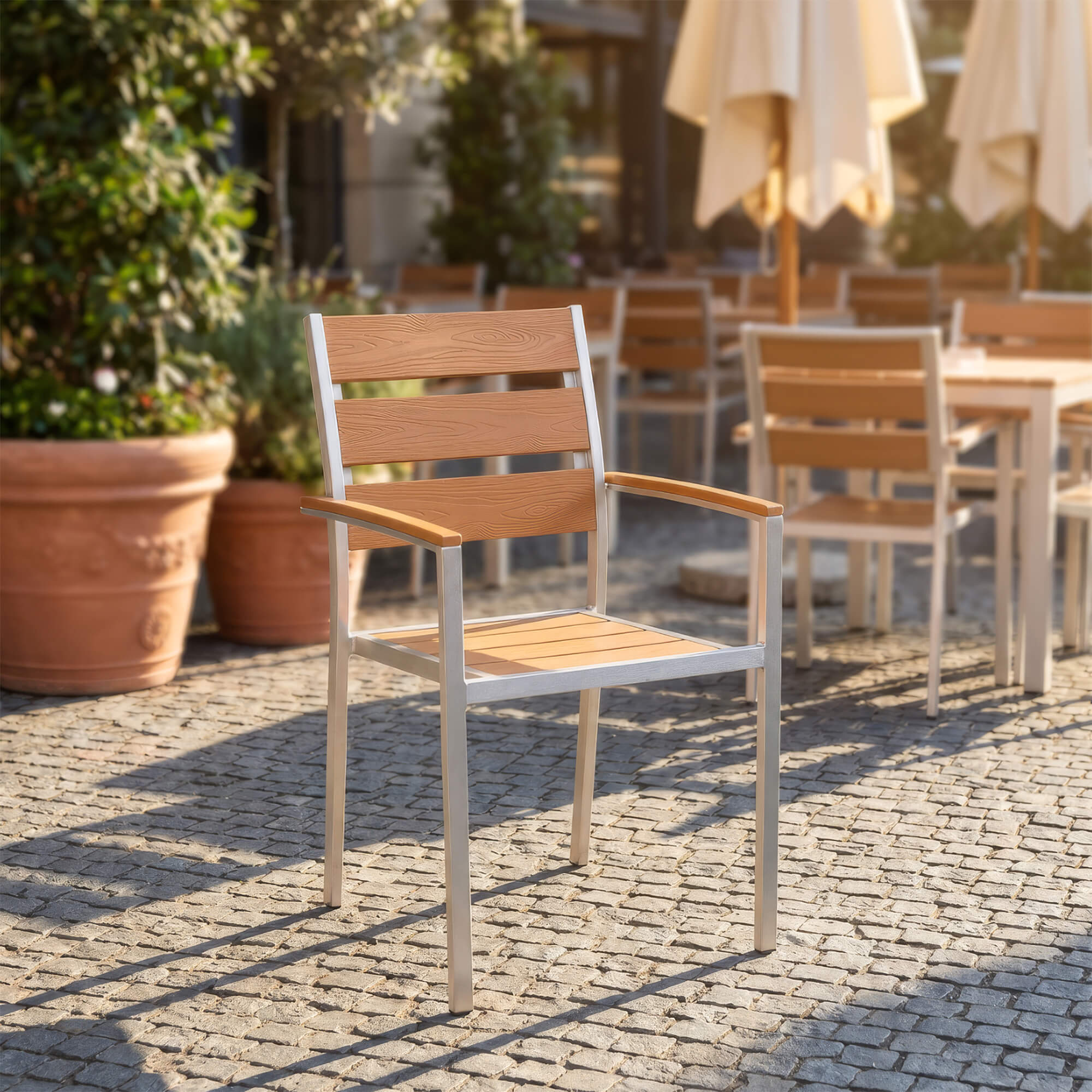 Stapelbarer Outdoorstuhl in Teak mit Armlehnen auf gepflasterter Terrasse