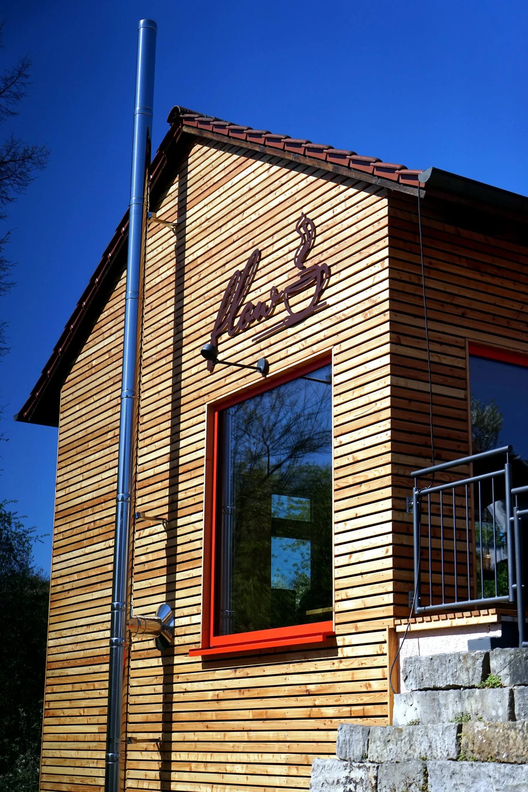 Aussenansicht des Cafe Flow in Marktgraitz mit Holzfassade und rotem Fensterrahmen